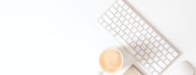 White desk with a keyboard and mouse, coffee, and notepad