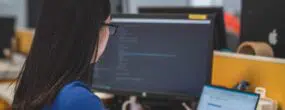 Woman working on code at a computer desk with two monitors