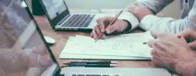 Two people working on laptops and reading notes